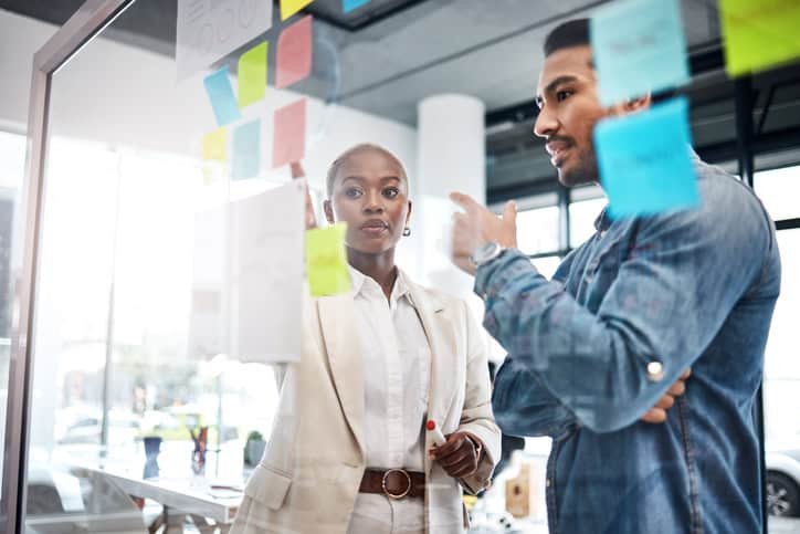 Creative People, Thinking And Meeting For Schedule Planning, Brainstorming Or Team Strategy At The Office. Man And Woman In Teamwork Decision For Project Plan, Tasks Or Sticky Note Ideas In Startup